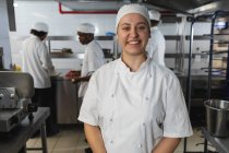Портрет кавказской женщины-шеф-повара с разнообразными коллегами на заднем плане. работа на кухне ресторана. — стоковое фото