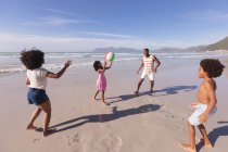 Afrikanisch-amerikanische Eltern und zwei Kinder beim Ballspielen am Strand. Familienfreizeit im Freien am Meer. — Stockfoto