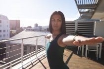 Mixed race transgender woman practicing yoga standing on roof terrace in the sun. staying at home in isolation during quarantine lockdown. — Stock Photo