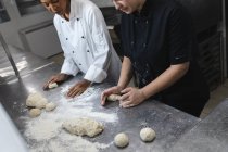 Професійні кухарі змішаної раси готують тісто на стільниці, покритому борошном. робота в зайнятій кухні ресторану . — стокове фото