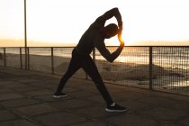 Homme afro-américain faisant de l'exercice à l'extérieur, s'étirant sur le pont au coucher du soleil. mode de vie sain en plein air entraînement fitness. — Photo de stock