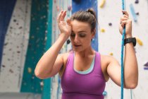 Caucasian woman taking rest rubbing her forehead at indoor climbing wall. fitness and leisure time. — Stock Photo