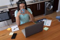 Змішана раса трансгендерна жінка працює вдома, використовуючи ноутбук, який п'є каву. перебування вдома в ізоляції під час карантину . — стокове фото