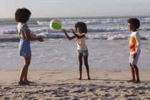 African american mother and two children playing with a ball at the beach. family outdoor leisure time by the sea. — Stock Photo