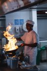 Piatto di flambeing del chef professionista afroamericano nel wok. lavorando in una cucina ristorante occupato. — Foto stock