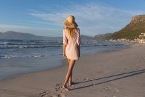 Kaukasische Frau mit Strandkleidung und Hut, die Spaß am Spazierengehen am Strand hat. gesunde Freizeit im Freien am Meer. — Stockfoto