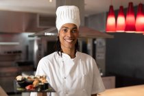 Портрет професійного шеф-кухаря змішаної раси в капелюсі кухарів, який подає суші. шеф-кухар на роботі на сучасній кухні ресторану . — стокове фото