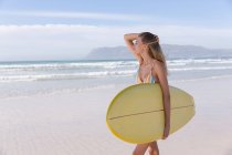 Caucasian woman wearing bikini carrying surfboard at the beach. healthy outdoor leisure time by the sea. — Stock Photo
