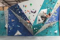 Mujer caucásica trepando por una pared en el gimnasio de escalada interior. fitness y tiempo libre en el gimnasio. - foto de stock