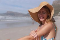 Kaukasische Frau im Bikini sitzt auf einem Handtuch und legt Sonnencreme auf den Strand. gesunde Freizeit im Freien am Meer. — Stockfoto