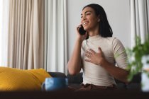Счастливая трансгендерная расовая женщина отдыхает в гостиной, сидя на диване и разговаривая по телефону. оставаться дома в изоляции во время карантинной изоляции. — стоковое фото