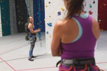 Duas mulheres caucasianas felizes conversando e se preparando para uma escalada na parede de escalada interior. fitness e tempo de lazer no ginásio. — Fotografia de Stock