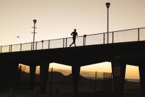 African american man exercising outdoors running on bridge at sunset. healthy outdoor lifestyle fitness training. — Stock Photo