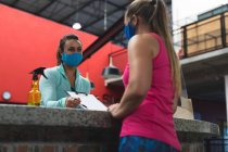 Kaukasische Frau mit Gesichtsmaske hinter Theke an der Rezeption des Fitness-Studios übergeben Dokument zu singen. Fitness und Freizeit im Fitnessstudio während der Coronavirus-Pandemie 19. — Stockfoto