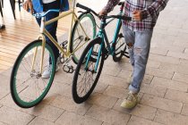 Sección media de dos amigos varones montando bicicletas en la calle. estilo de vida urbano verde, fuera y alrededor de la ciudad. - foto de stock