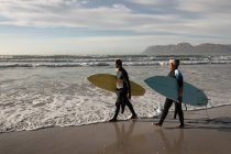 Couple afro-américain senior transportant des planches de surf marchant sur la plage. voyage vacances retraite style de vie concept — Photo de stock