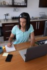 Mulher transgênero de raça mista trabalhando em casa usando laptop fazendo anotações. ficar em casa em isolamento durante o confinamento de quarentena. — Fotografia de Stock