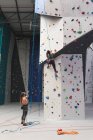 Two caucasian women wearing face masks using ropes to climb wall at indoor climbing gym. fitness and leisure time at gym during coronavirus covid 19 pandemic. — Stock Photo