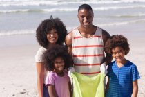 Батьки-афроамериканці з двома дітьми збирають сміття з пляжу, посміхаючись. родинний догляд на пляжі. — стокове фото