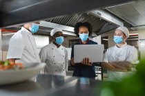 Diversi gruppi di chef professionisti che si incontrano con il direttore della cucina indossando maschere facciali. lavorando in una cucina ristorante occupato durante coronavirus covid 19 pandemia. — Foto stock