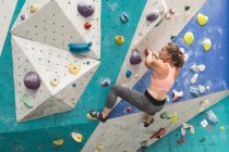 Кавказька жінка піднімається вгору по стіні в приміщенні спортивного залу. Фізкультура та вільний час у спортзалі. — стокове фото