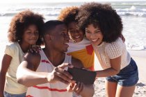 Батьки-афроамериканці та двоє дітей, які роблять селфі зі смартфоном на пляжі, посміхаються. сім'я на відкритому повітрі відпочиває біля моря. — стокове фото