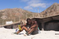 Африканский американец занимается спортом, отдыхает на пляже, держит бутылку в солнечный день. фитнес-тренировки. — стоковое фото