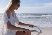 Белая женщина на велосипеде на пляже. здоровый отдых на открытом воздухе у моря. — стоковое фото