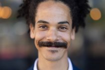 Portrait of mixed race male with moustache looking to camera and smiling. independent small business in a city. — Stock Photo