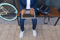 Der mittlere Teil der Männer sitzt auf einer Bank auf der Straße und benutzt einen Laptop. digitaler Nomade, unterwegs in der Stadt. — Stockfoto