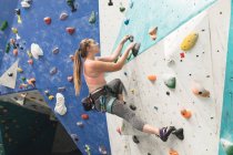 Kaukasische Frau klettert in einer Kletterhalle eine Wand hinauf. Fitness und Freizeit im Fitnessstudio. — Stockfoto
