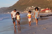 Усміхнені афроамериканські батьки і двоє дітей ходять і тримають руки на пляжі. сім'я відпочинок на відкритому повітрі час на морі . — стокове фото