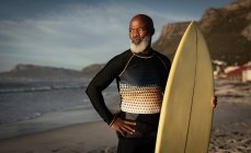 Retrato do afro-americano idoso na praia segurando prancha de surf com vista para o mar. saúde e bem-estar, reforma activa. — Fotografia de Stock