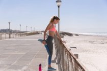 Caucasian woman exercising stretching on a promenade by the beach. healthy outdoor leisure time by the sea. — Stock Photo