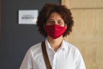 Portrait of mixed race man wearing face mask standing in hotel lobby with shoulder bag. business travel hotel during coronavirus covid 19 pandemic. — Stock Photo