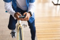 Seção média de homem sentado na bicicleta na rua usando smartphone. nômade digital, para fora e sobre na cidade. — Fotografia de Stock