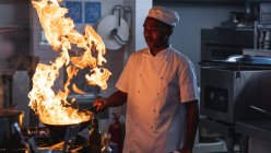 Piatto di flambeing del chef professionista afroamericano nel wok. lavorando in una cucina ristorante occupato. — Foto stock