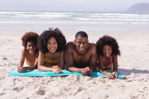 Портрет батьків-афроамериканців і двоє дітей лежали на рушнику, усміхаючись на пляжі. сім'я на відкритому повітрі відпочиває біля моря. — стокове фото