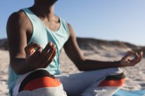 Sección media del hombre afroamericano haciendo ejercicio al aire libre, practicando yoga, meditando en la playa. estilo de vida al aire libre saludable entrenamiento fitness. - foto de stock