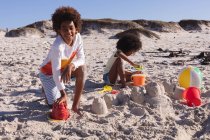African american children having fun playing with sand at the beach. family outdoor leisure time by the sea. — Photo de stock