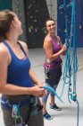 Zwei glückliche kaukasische Frauen unterhalten sich und bereiten sich auf einen Aufstieg an einer Indoor-Kletterwand vor. Fitness und Freizeit im Fitnessstudio. — Stockfoto