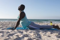 Relaxado homem afro-americano exercitando ao ar livre, praticando ioga na praia. treinamento de fitness ao ar livre saudável. — Fotografia de Stock