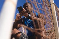 Афроамериканець займається фізичними вправами, носить навушники, користується смартфоном у сонячний день. здорове тренування на відкритому повітрі. — стокове фото