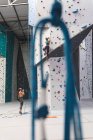 Dos mujeres caucásicas que usan máscaras faciales usando cuerdas para escalar la pared en el gimnasio de escalada interior. fitness y tiempo libre en el gimnasio durante coronavirus covid 19 pandemia. - foto de stock