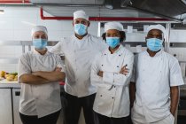 Ritratto di diversi chef professionisti di razza maschile e femminile in piedi in maschere facciali. lavorando in una cucina ristorante occupato durante coronavirus covid 19 pandemia. — Foto stock