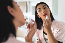 Mixed race transgender woman looking in bathroom mirror and putting on lipstick. staying at home in isolation during quarantine lockdown. — Stock Photo