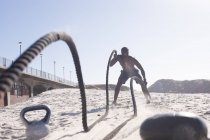 Afrikanisch-amerikanischer Mann, der am Strand mit Seil und Wasserkocher trainiert. gesundes Outdoor-Fitness-Training. — Stockfoto