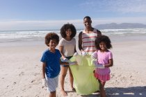 Afrikanische amerikanische Eltern mit zwei Kindern, die lächelnd Müll am Strand sammeln. Öko-Strandschutz für Familien. — Stockfoto