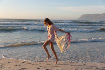 Bella donna caucasica tenendo sciarpa a piedi e godendo in spiaggia. estate concetto di vacanza al mare. — Foto stock