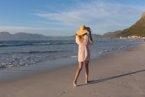 Caucasian woman wearing beach cover up and hat having fun walking at the beach. healthy outdoor leisure time by the sea. — Photo de stock